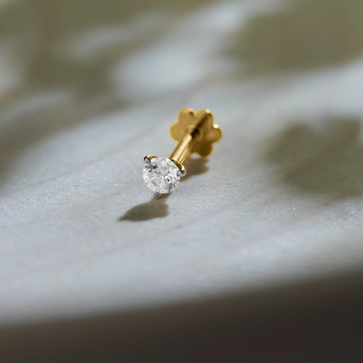 Round solitaire diamond stud earring with prong setting on marble background