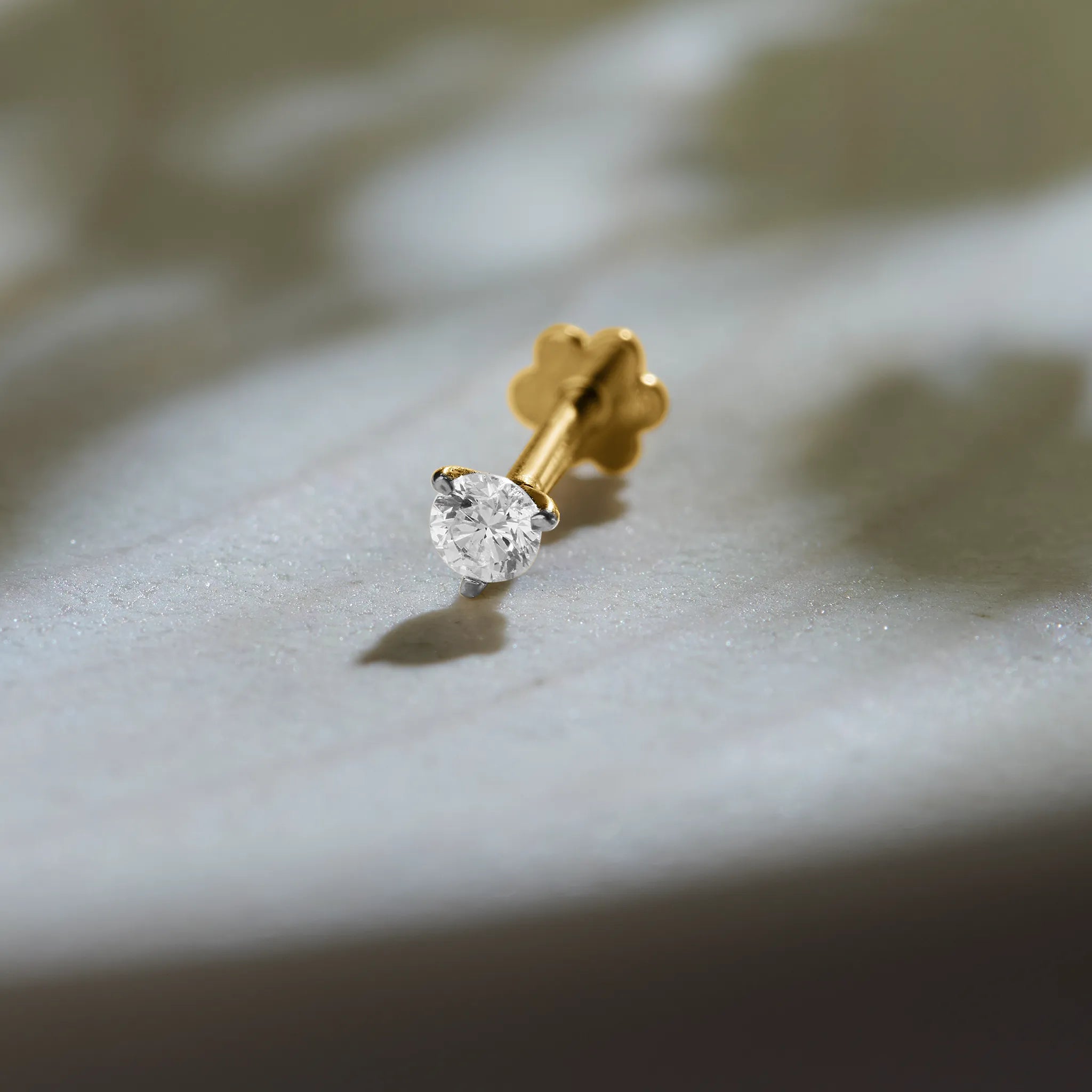 Round solitaire diamond stud earring with prong setting on marble background