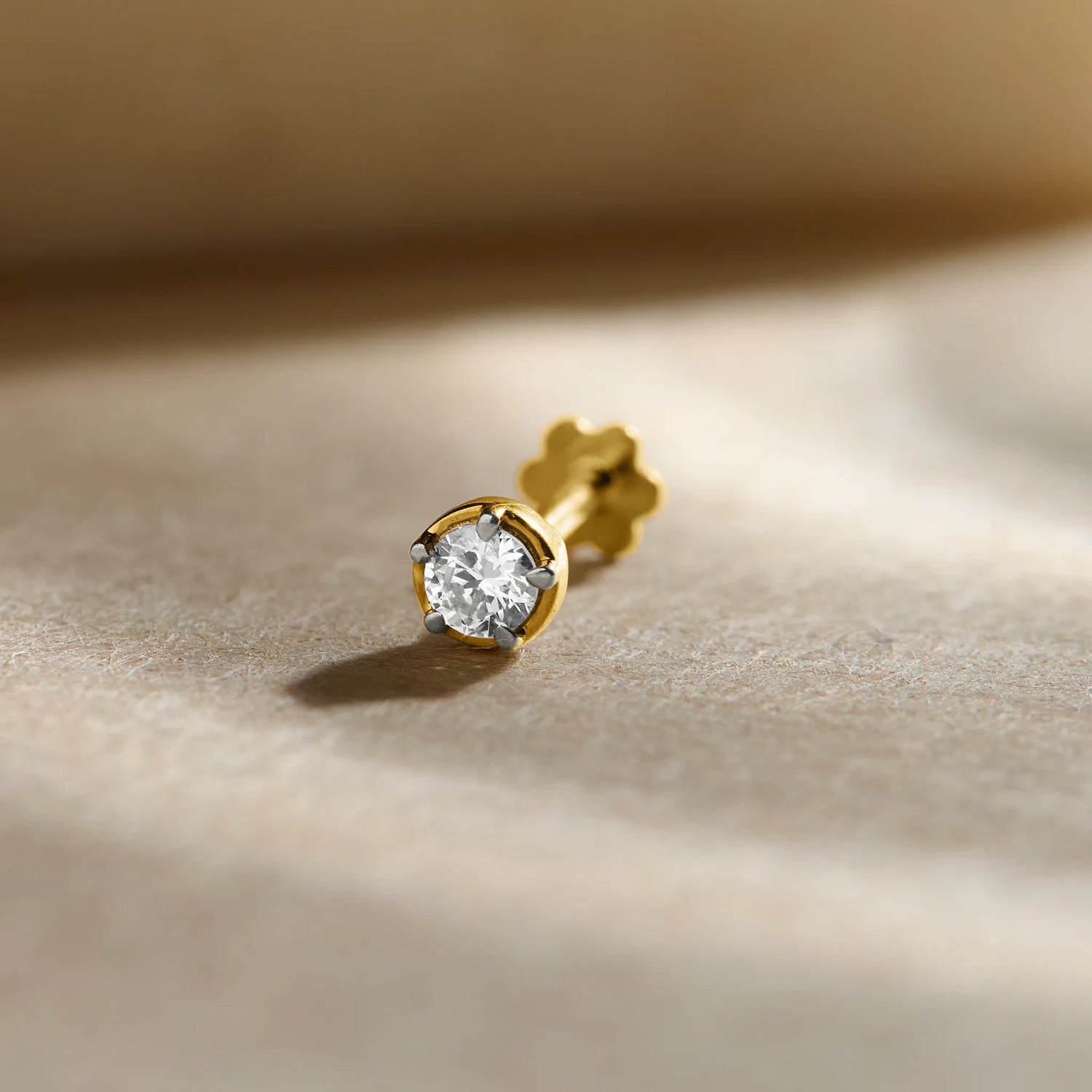 Diamond nose pin design from Kerala in gold with a classic solitaire diamond setting in a polished gold base on a soft neutral background