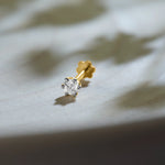 Round diamond stud earring in 14k gold with prong setting on marble background
