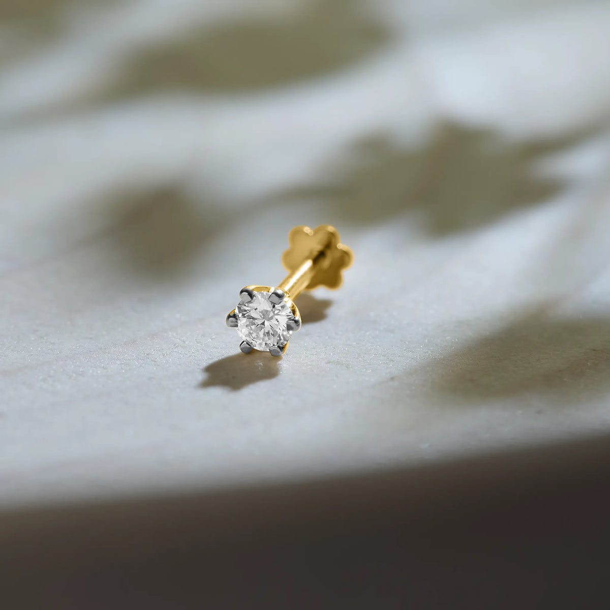Round diamond stud earring in 14k gold with prong setting on marble background
