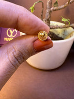 Round textured gold nose pin with raised heart center, held between fingertips