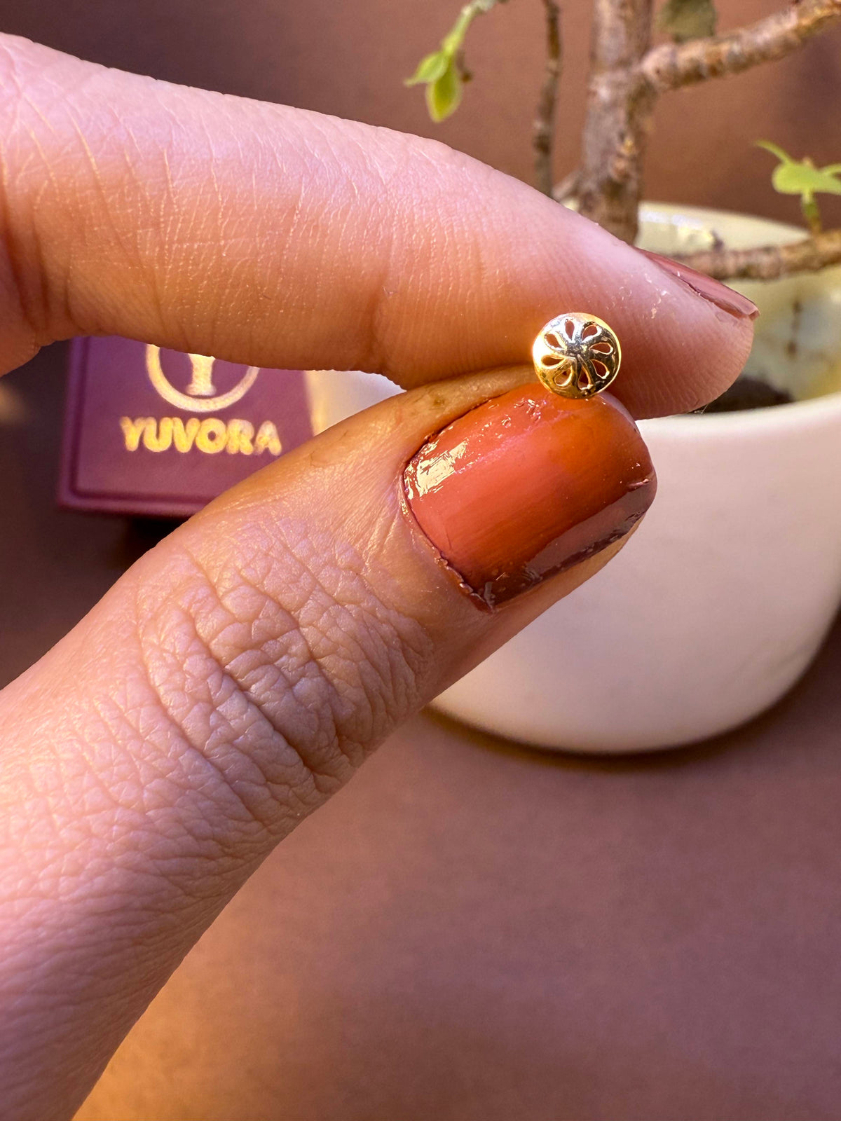 Smooth domed gold nose pin with starburst pattern, held between fingertips