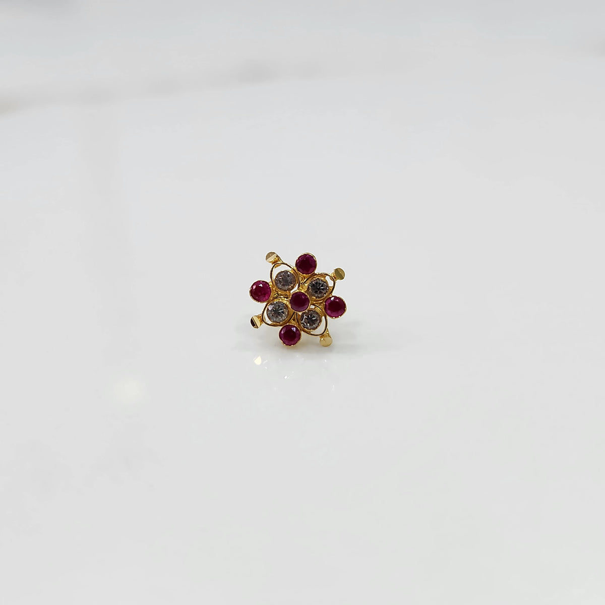 A gold nose pin shaped like a flower, set with ruby-red and clear crystal stones