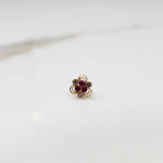 An 18K gold nose pin shaped like a flower, set with ruby-red and clear crystal stones in open gold loops