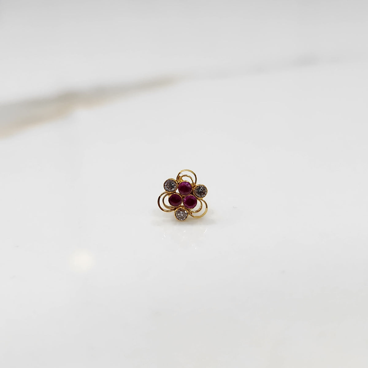 An 18K gold nose pin shaped like a flower, set with ruby-red and clear crystal stones in open gold loops