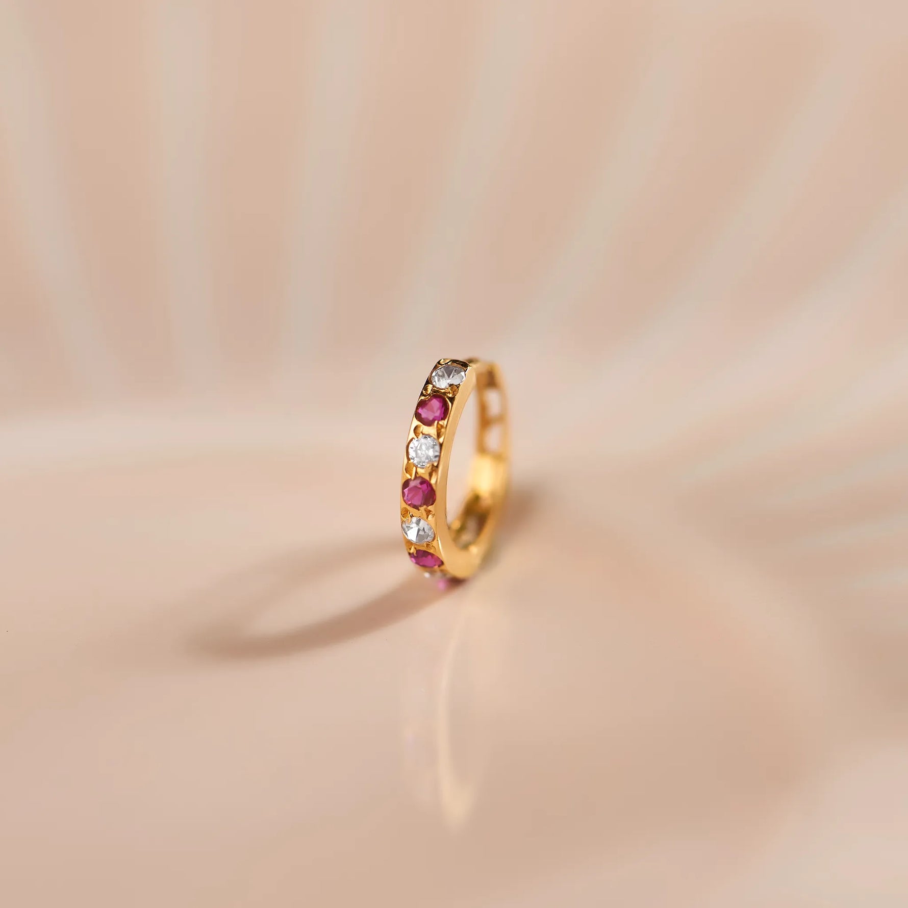 Close up of gemstone studded gold nose ring placed on a soft peach toned surface with elegant radial background