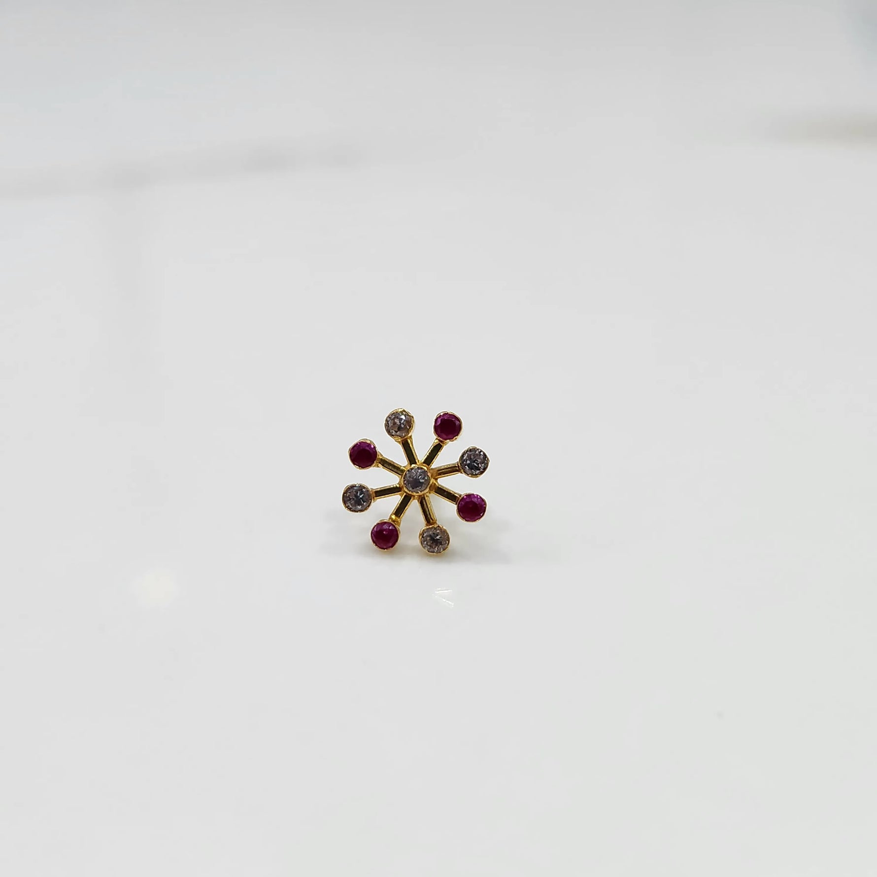 Product shot of a gold nose stud with alternating ruby and diamond stones
