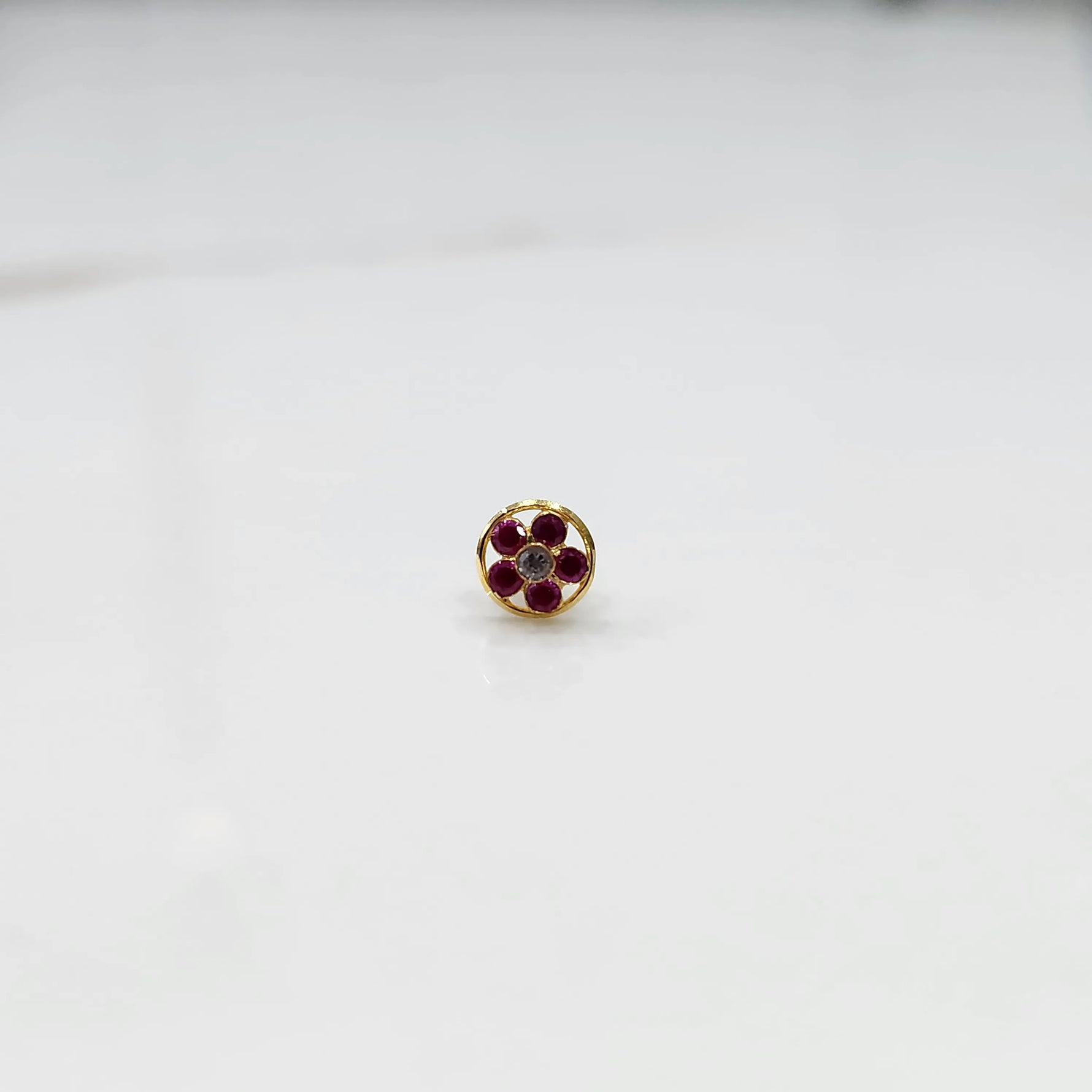 Ruby flower cluster nose stud with round gold border, jewelry photography