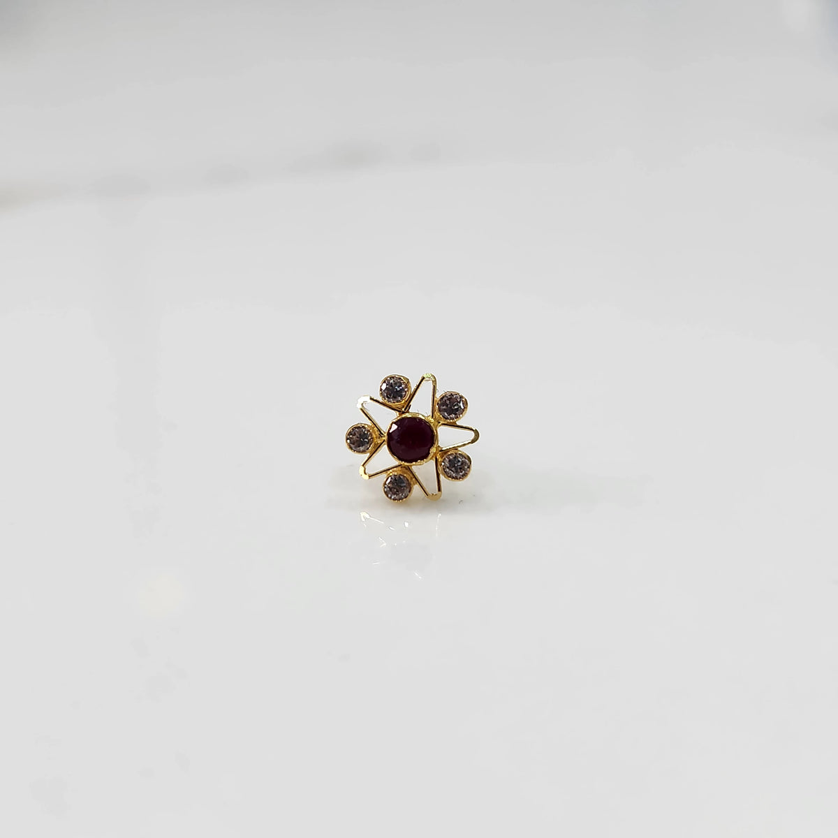 A gold nose pin shaped like a star with a round deep red center stone and clear crystal accent stones 