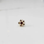 A gold nose pin shaped like a star with a round deep red center stone and clear crystal accent stones 