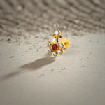 An 18K gold nose pin shaped like a flower with a red center stone and clear crystal petals, with a small crystal accent above