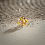 An 18K gold nose pin shaped like a flower with open gold petal outlines, set with clear crystal stones, photographed on a light textured surface