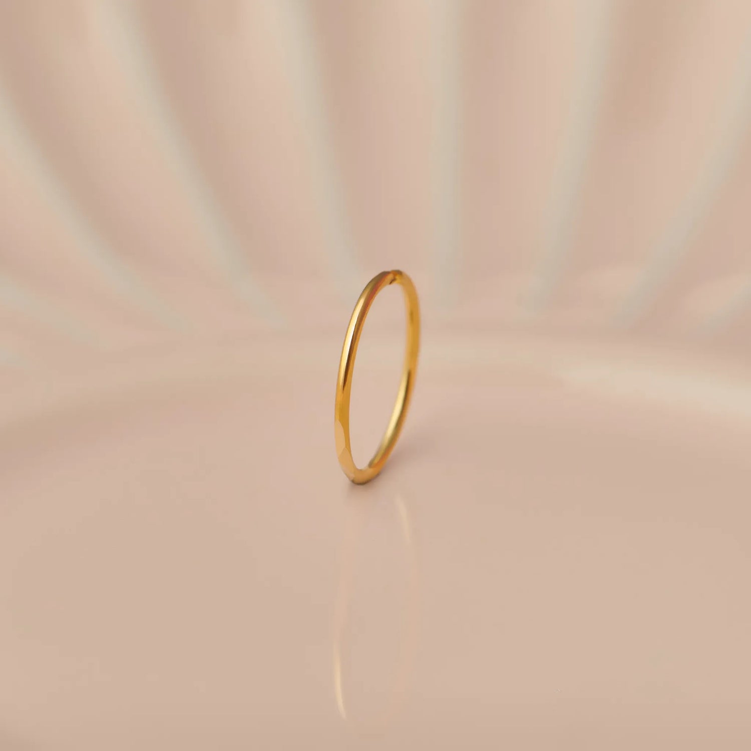 Front view of slim plain 18K gold hoop nose ring standing upright on a soft beige background with subtle light reflections
