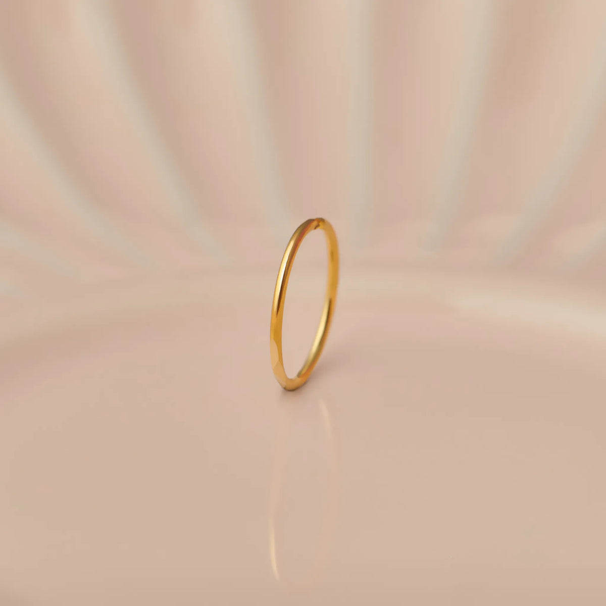 Front view of slim plain 18K gold hoop nose ring standing upright on a soft beige background with subtle light reflections