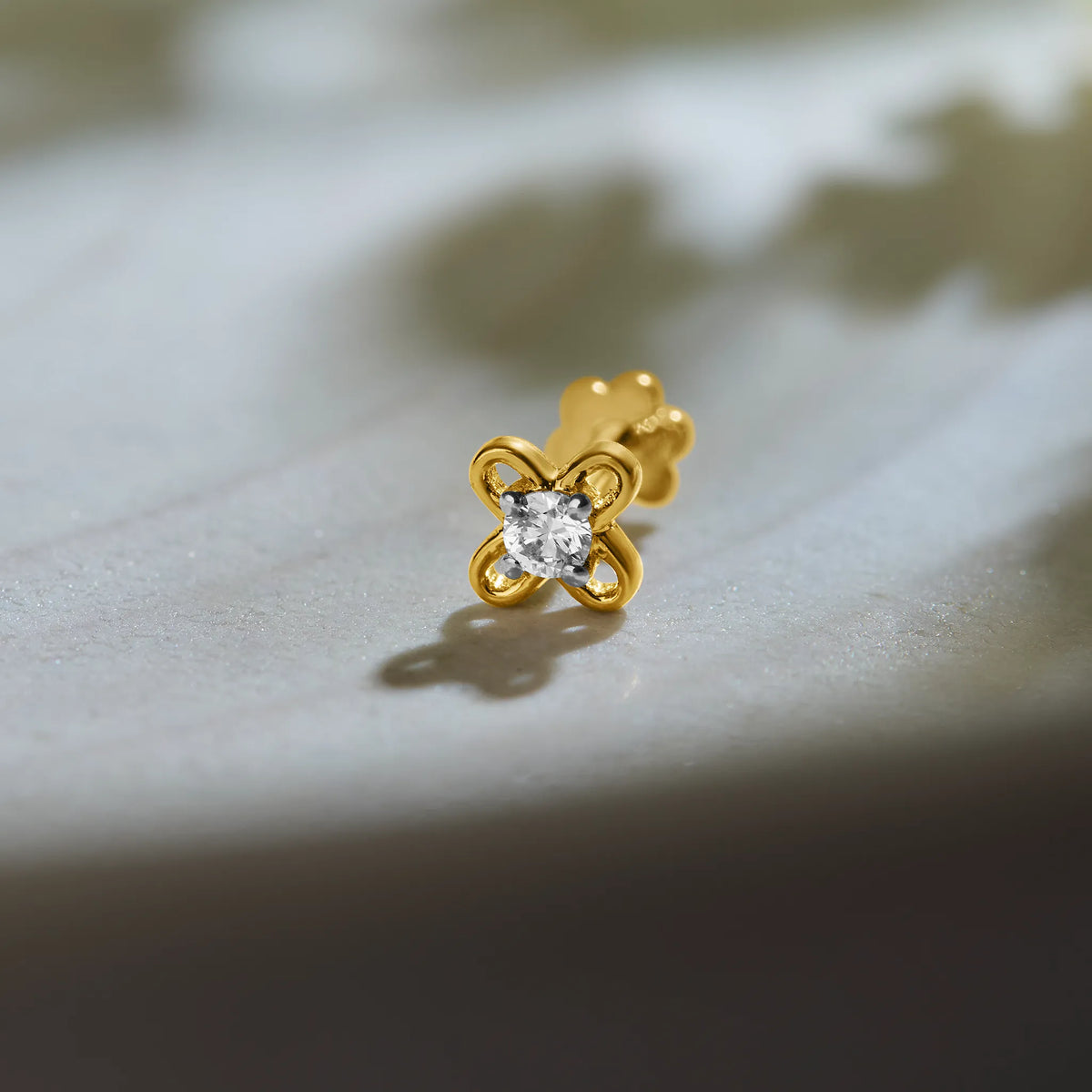 Flower gold nose pin with diamond design on soft textured background
