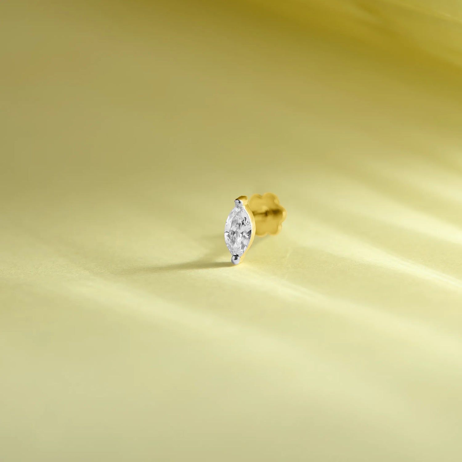Single stone nose pin gold with marquise diamond solitaire design on soft yellow background