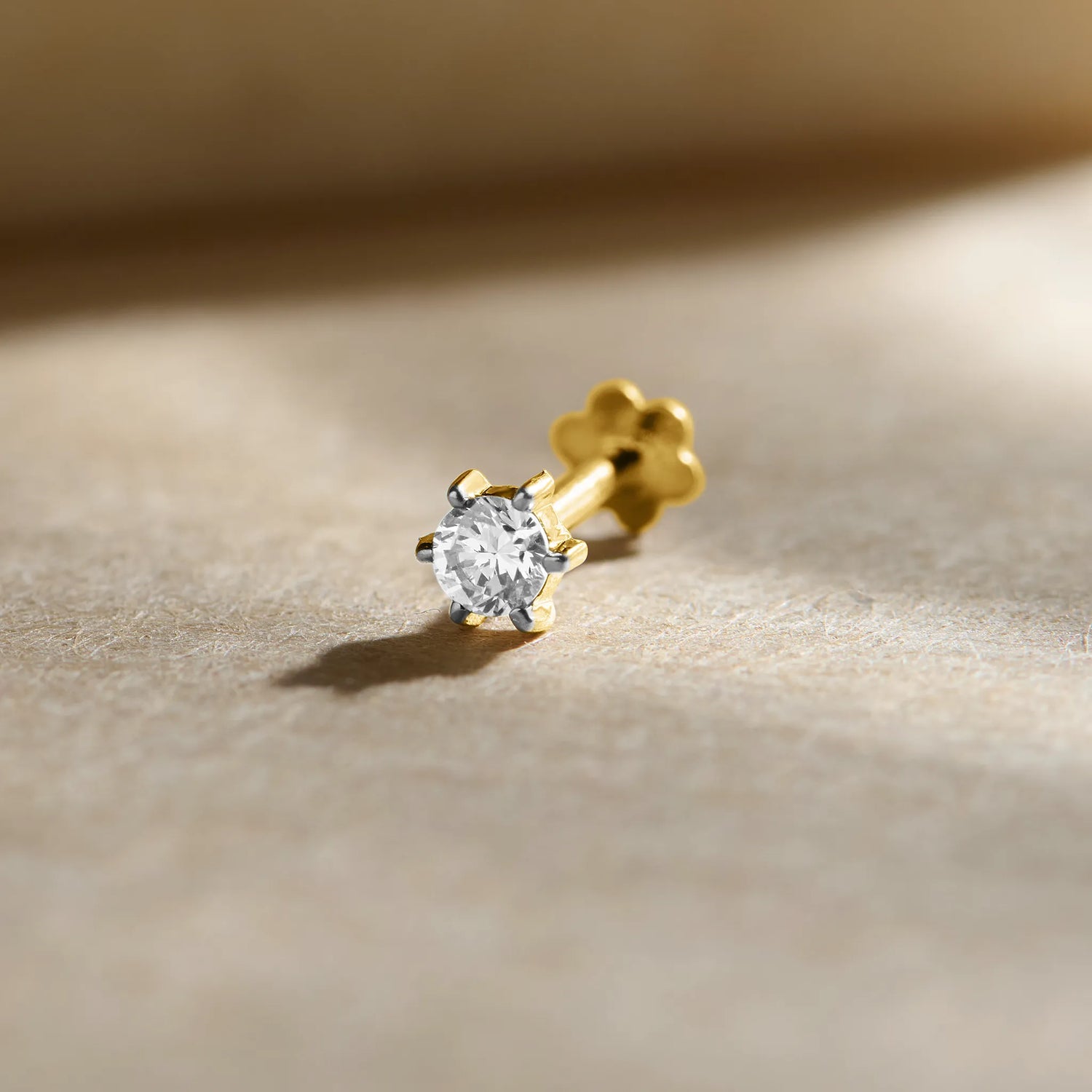 Diamond nose pin design from Kerala in gold with a sparkling solitaire diamond set in a polished gold prong setting on a soft neutral background