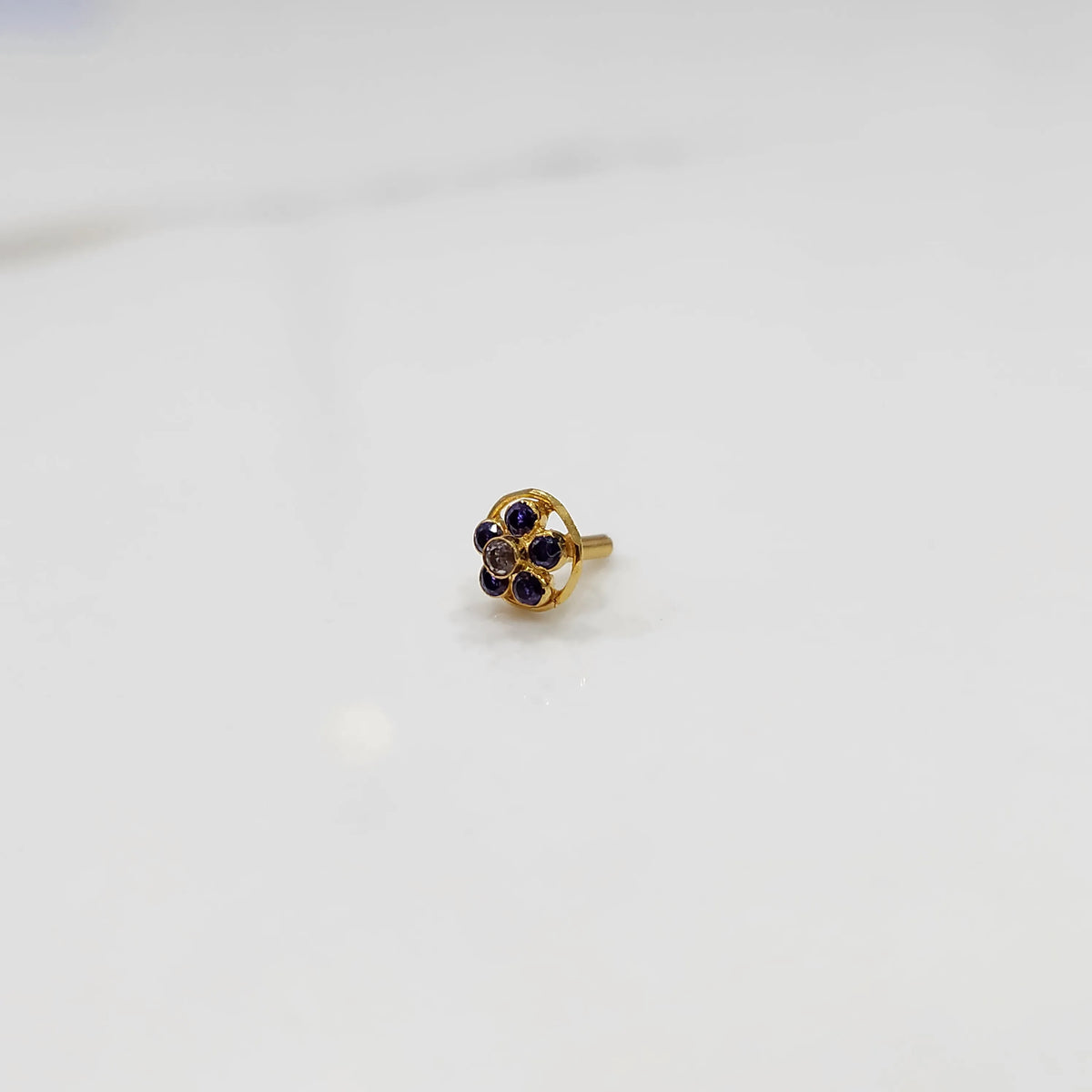 Close-up of a six-stone blue gemstone nose pin in round gold halo setting