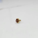 Product shot of a round gold nose stud with ruby red gemstone flower cluster