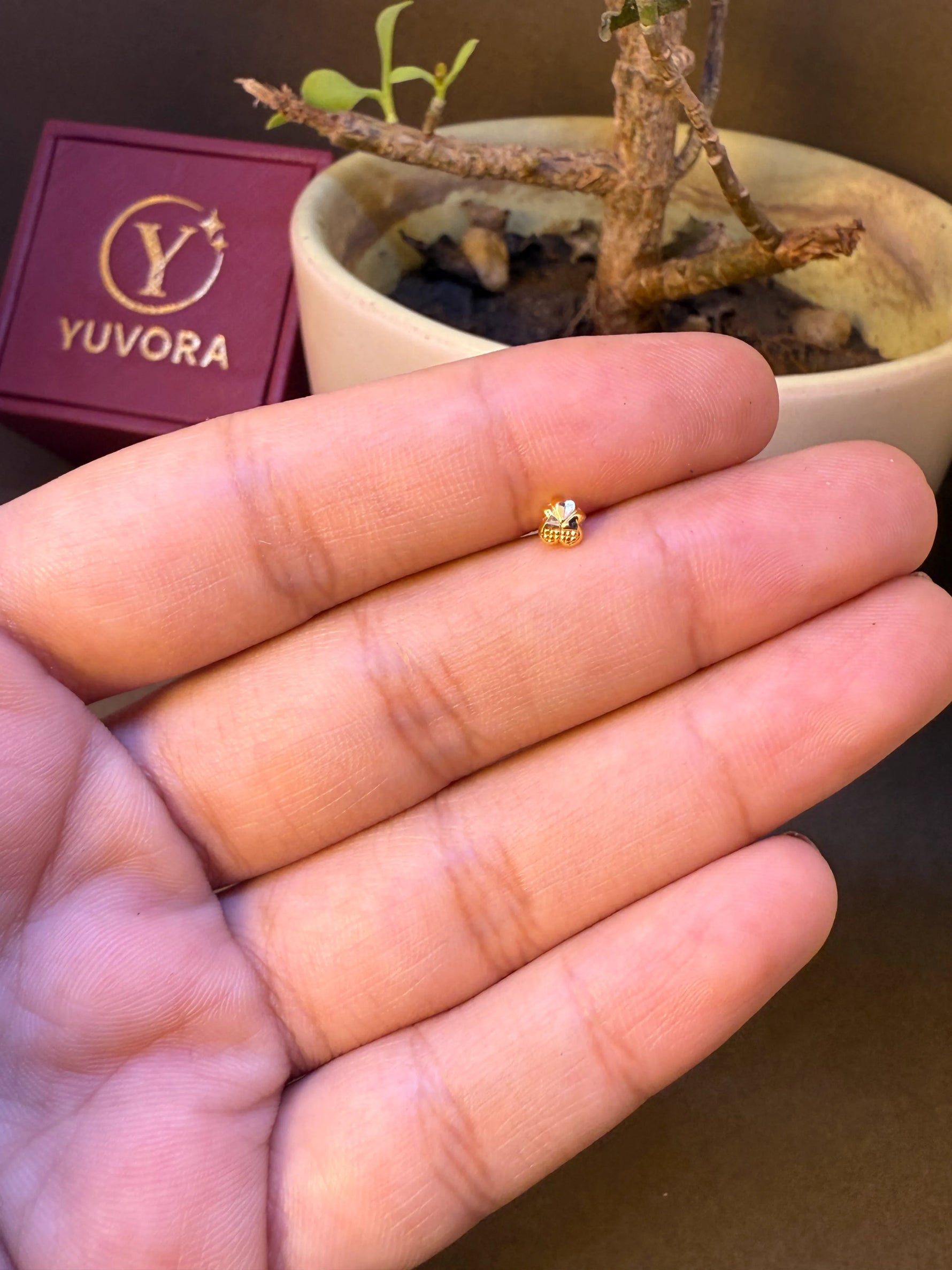 Tiny bud-shaped gold nose pin with textured finish, held in hand