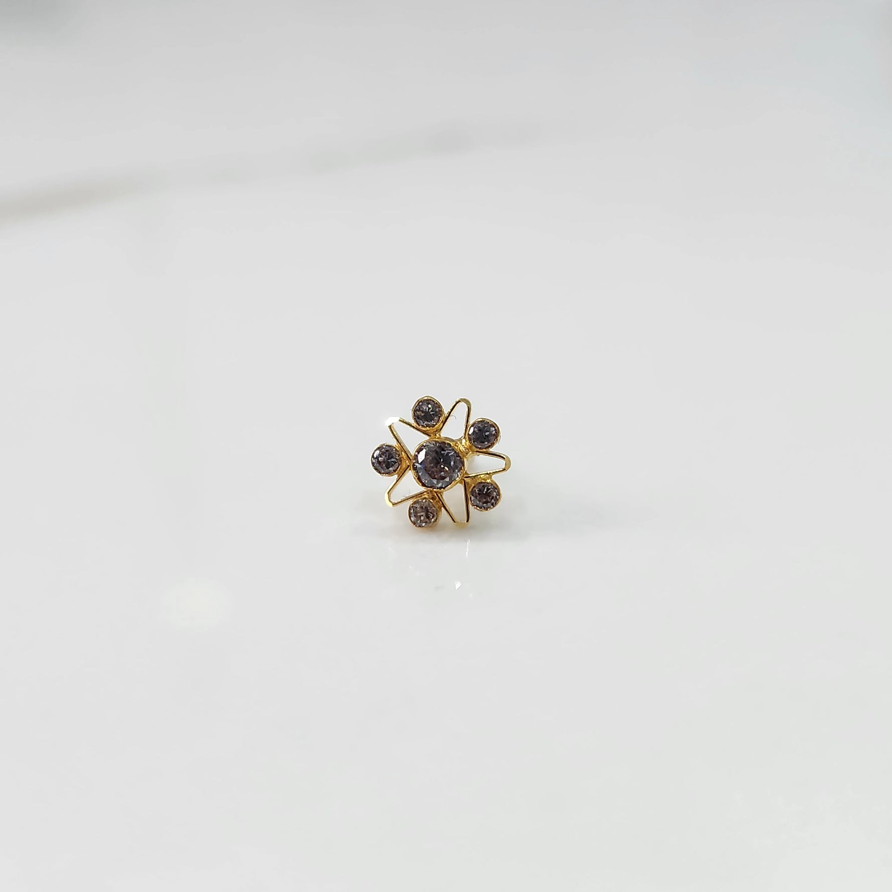 A gold nose pin shaped like a star, set entirely with smoky grey crystal stones