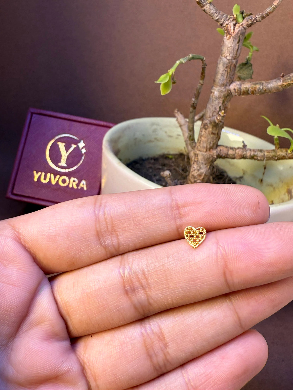 Solid heart-shaped gold nose pin with textured surface, held in hand