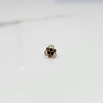 An 18K gold nose pin shaped like a flower, set with black and lavender-grey stones in open gold loops, close-up view