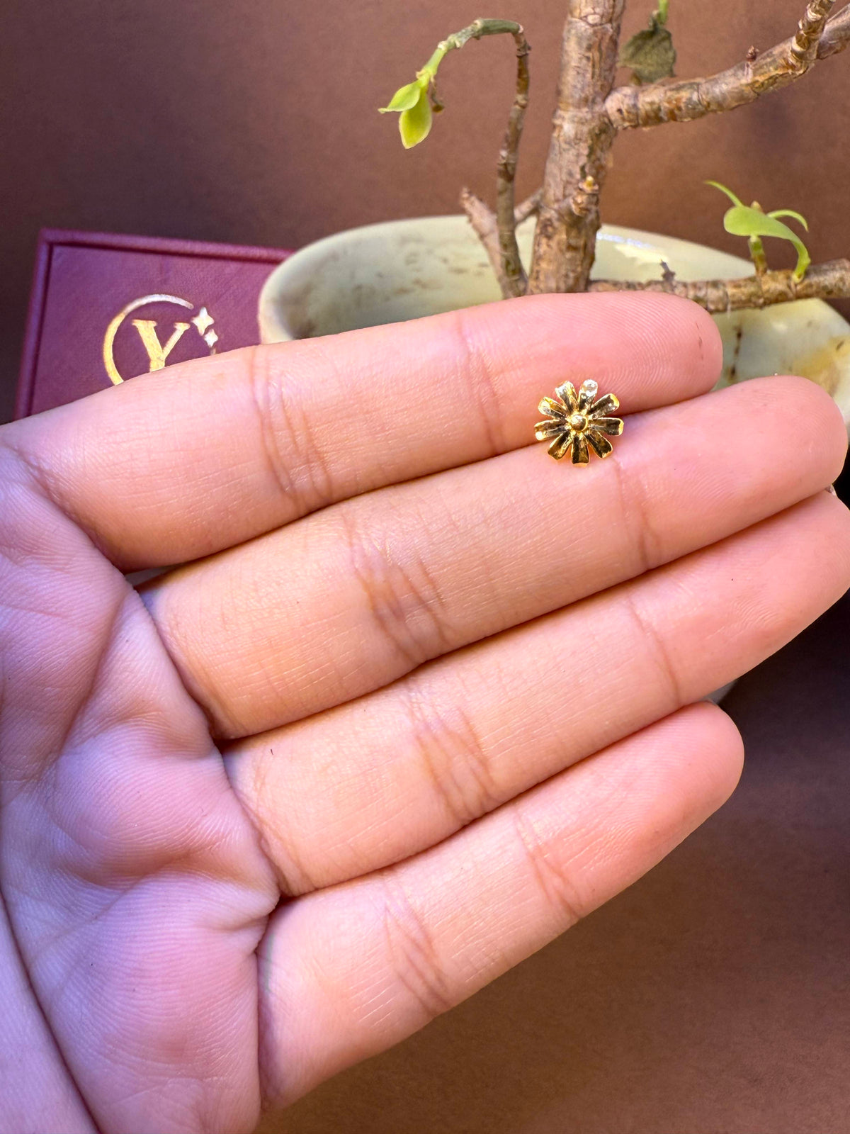 Sunflower-shaped gold nose pin with ridged petals and center stone, held in hand
