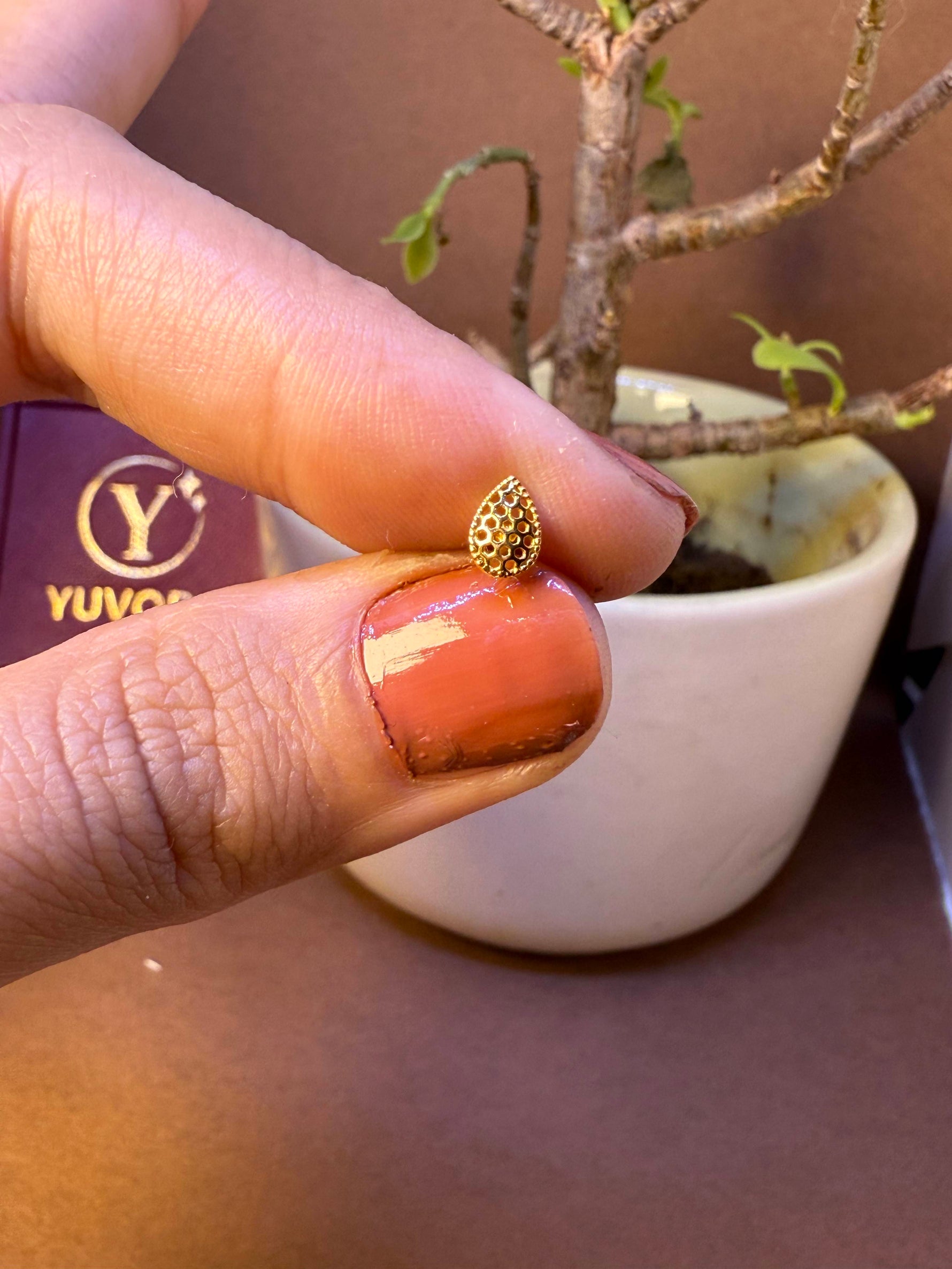 Teardrop-shaped gold nose pin with beaded texture, held between fingertips