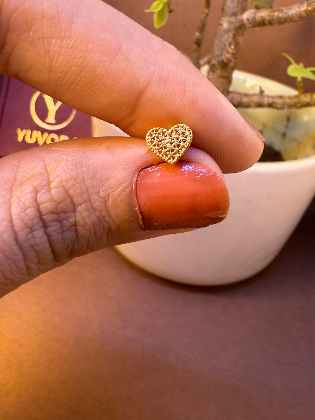 Heart-shaped gold nose pin with stippled texture, held between fingertips