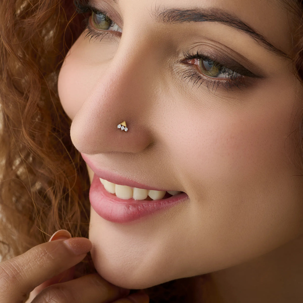 Close-up of woman wearing a gold nose stud with a three-diamond cluster