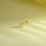 Round gold nose pin with three sparkling white stones on a soft pastel green background.