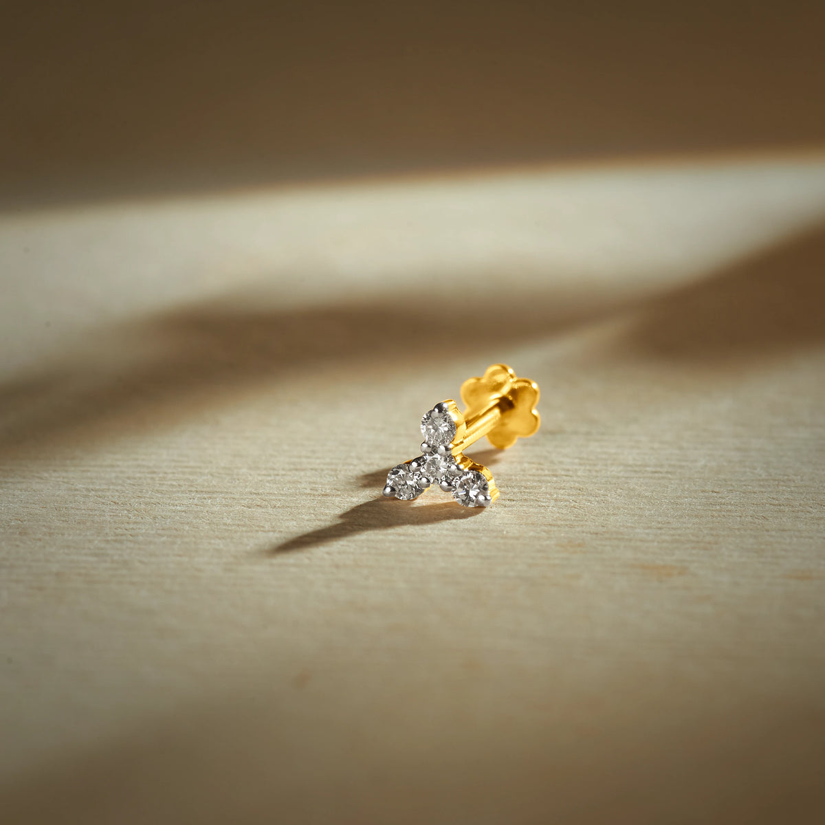 Nose pin gold with delicate leaf-inspired design featuring sparkling stones set in a polished gold base on a soft neutral background