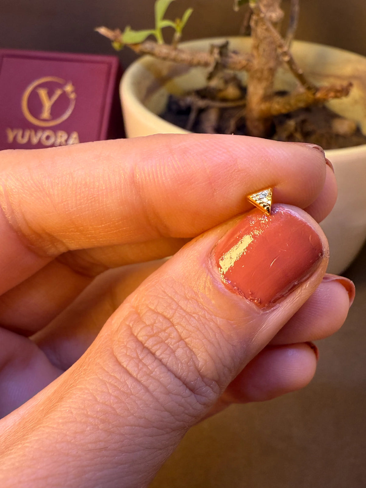 Triangle-shaped gold nose pin with textured surface, held between fingertips