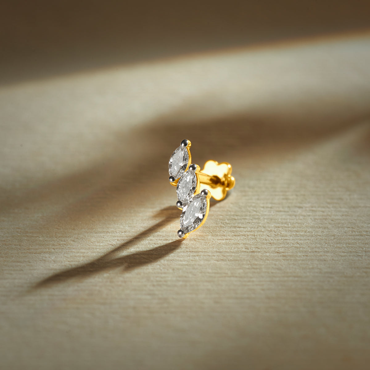 Gold nose pin with double leaf design featuring sparkling stones set in a polished gold base on a soft neutral background