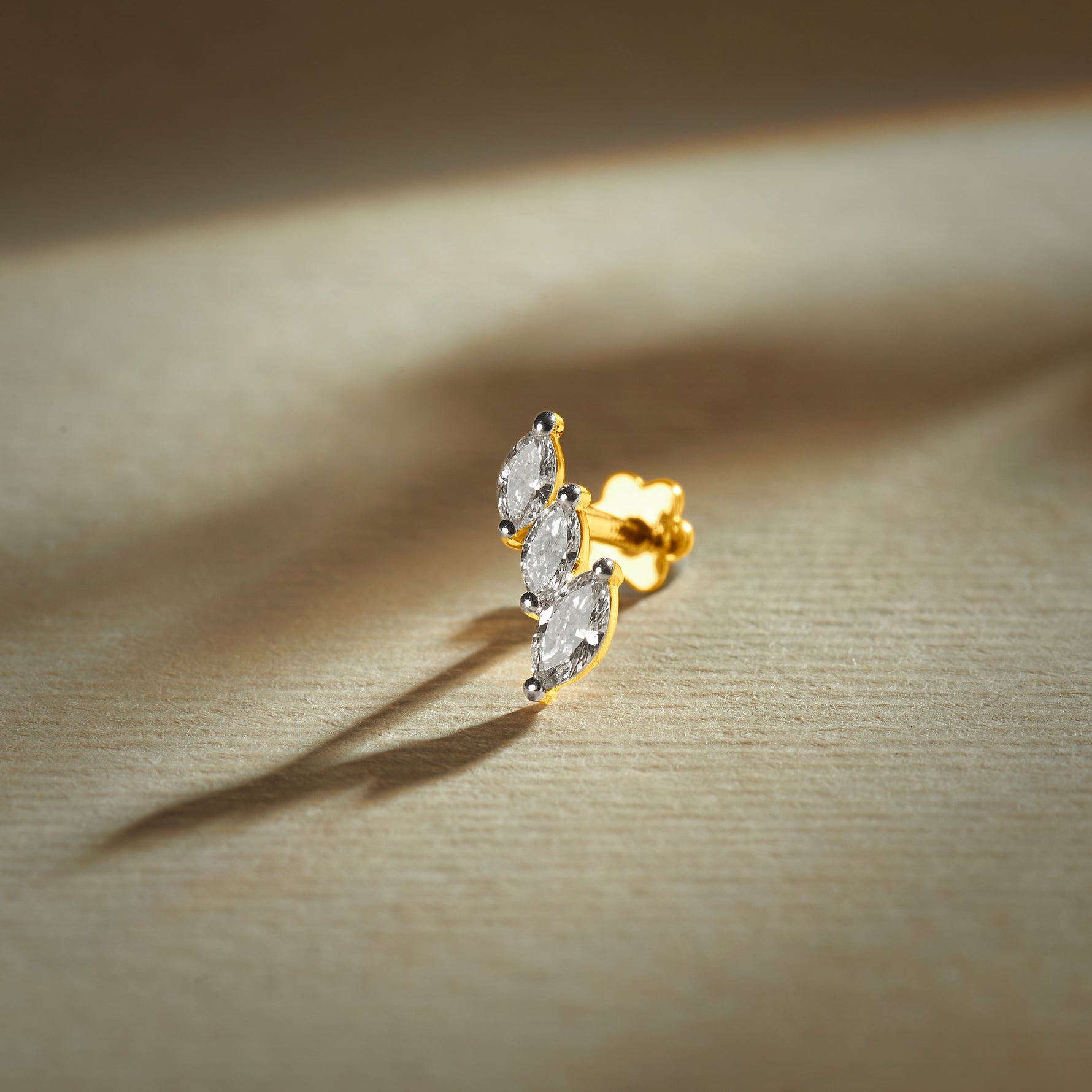 Gold nose pin with double leaf design featuring sparkling stones set in a polished gold base on a soft neutral background