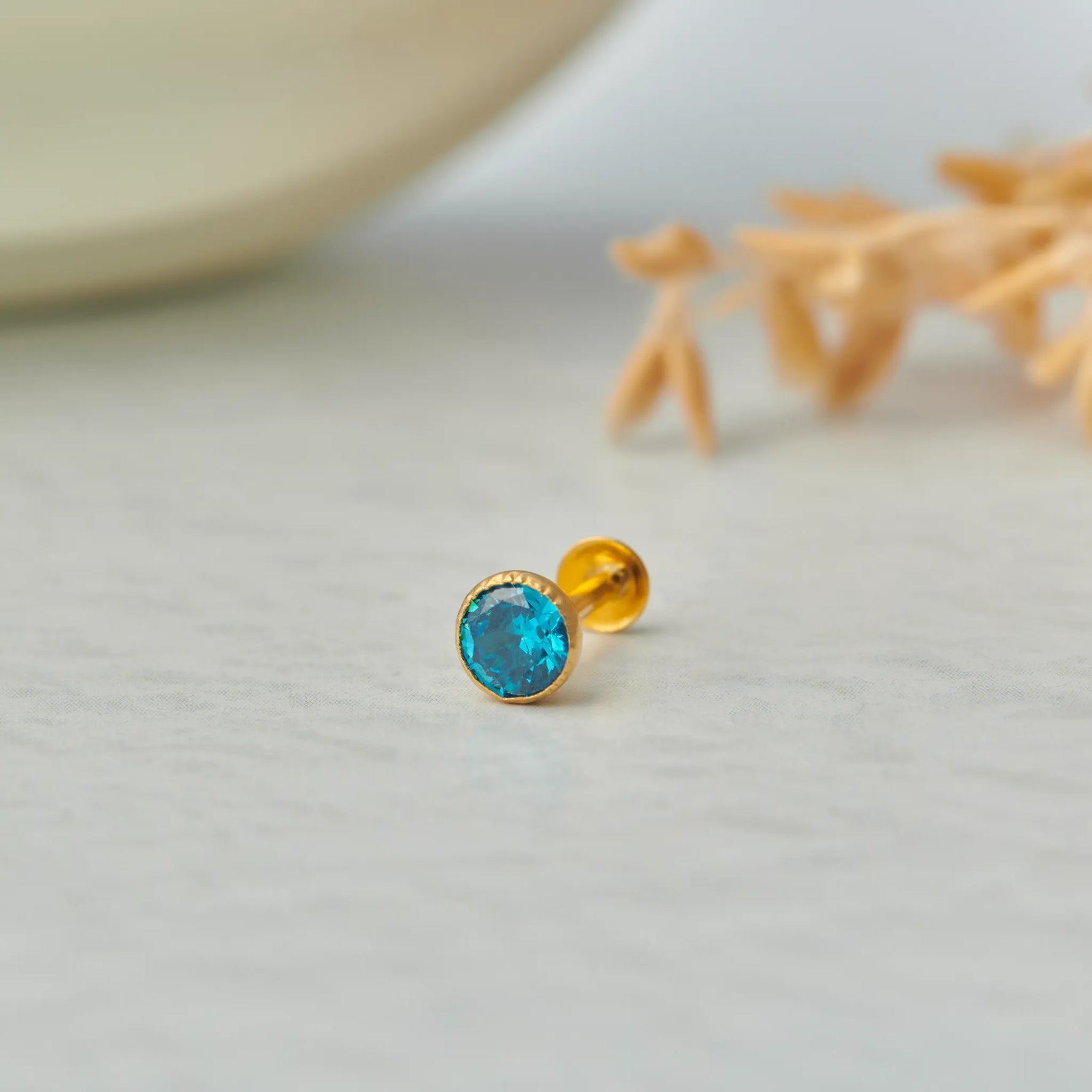 Gold stone nose pin with blue gemstone placed on light surface