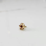 An 18K gold nose pin shaped like a star with a ruby-red center stone and light pink accent stones, photographed on a plain white background
