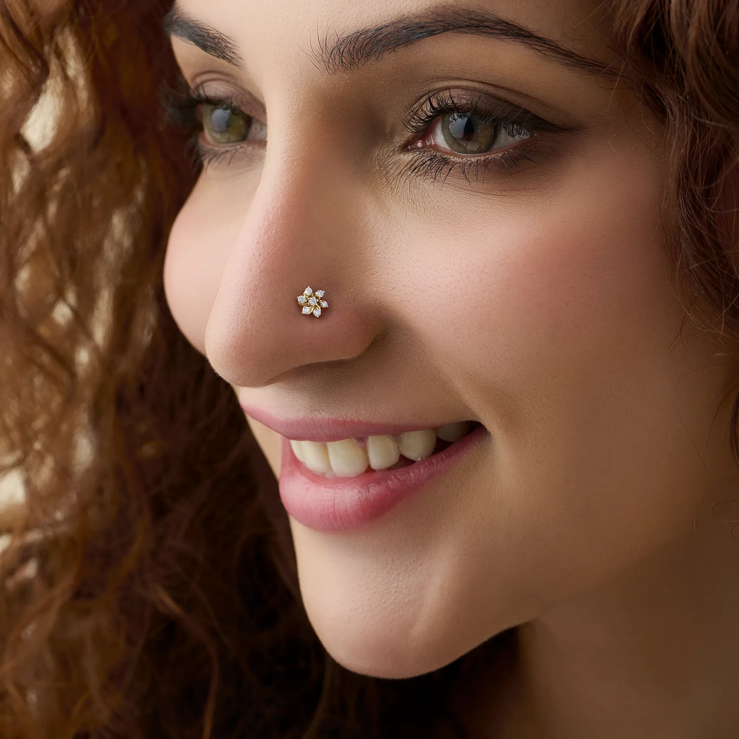 Gold snowflake diamond nose stud worn by a smiling woman, close-up beauty shot