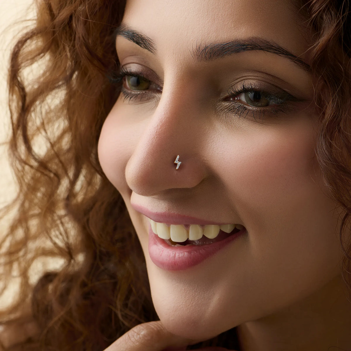Lightning bolt nose stud worn by a smiling woman, close-up beauty shot