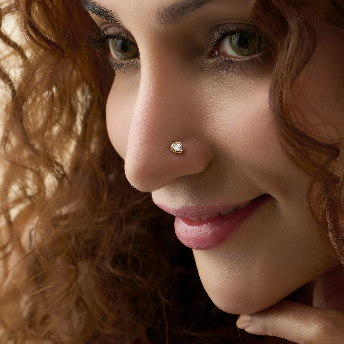 Triangle diamond nose stud worn by a smiling woman, close-up beauty shot