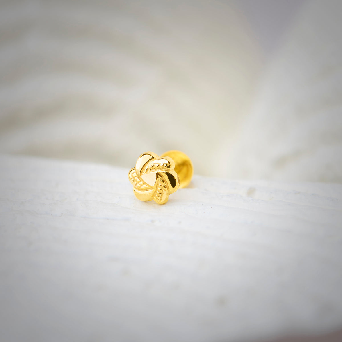 Front view of knot-shaped 18K nose pin gold placed on a soft white surface highlighting its detailed textured design