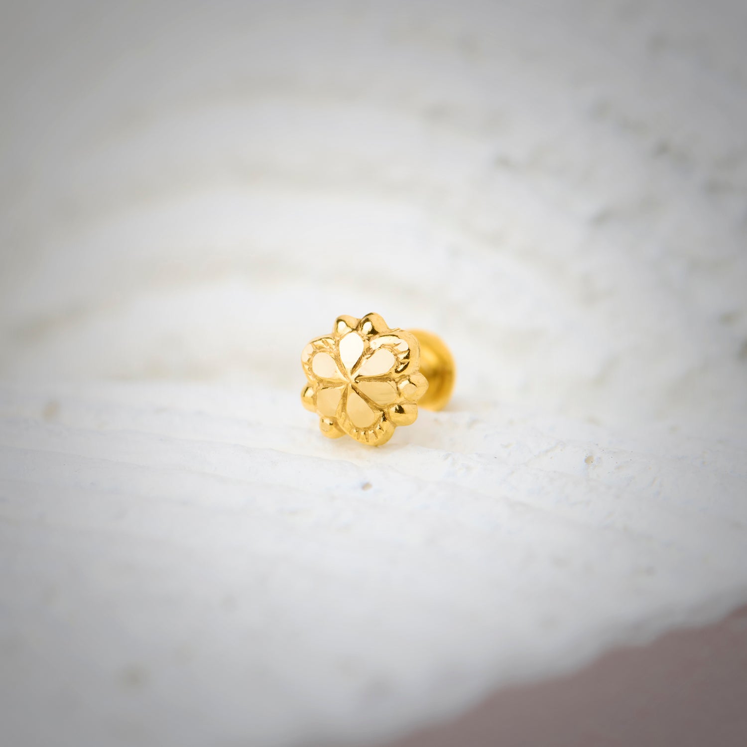 Close-up of floral-shaped 18K nose pin gold placed on a soft white surface highlighting its intricate detailing