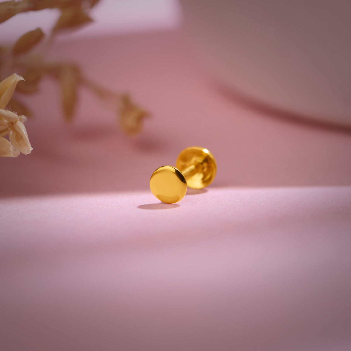 Minimal 18k gold round stud nose pin displayed on soft pink background for aesthetic product showcase