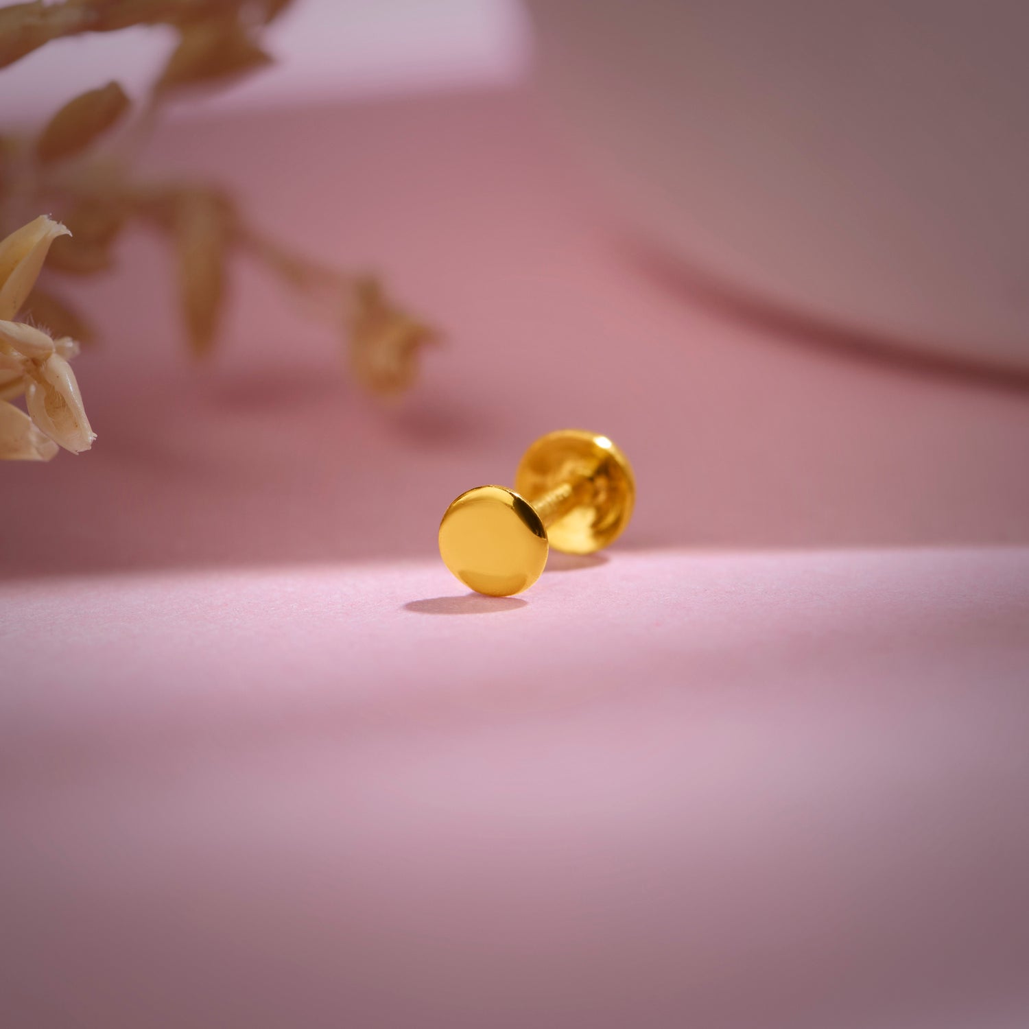 Minimal 18k gold round stud nose pin displayed on soft pink background for aesthetic product showcase