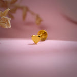 Close-up of heart-shaped 18K nose pin gold placed on a soft pink surface highlighting its smooth polished finish